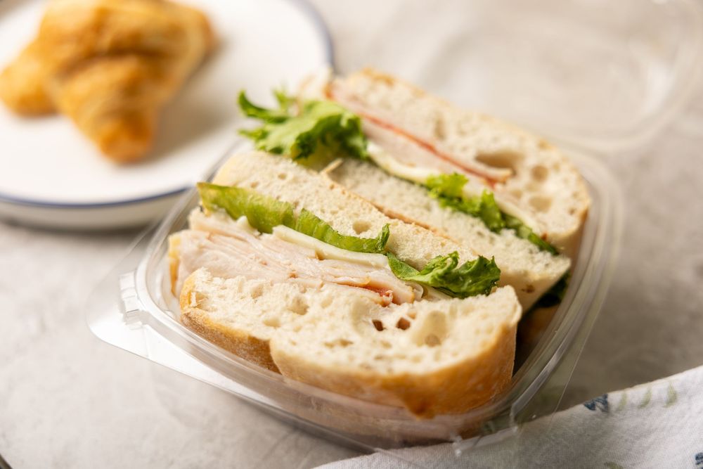 Classic deli sandwich with turkey, lettuce and tomato served on sliced white bread in a plastic container.
