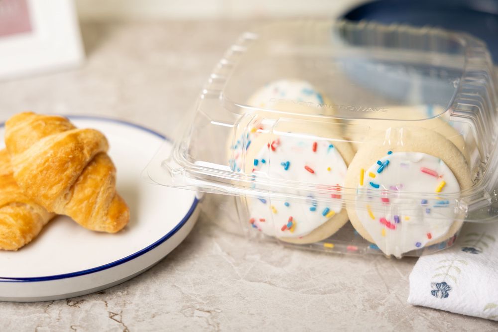 White frosted cake pops with colorful sprinkles in a clear container next to a flaky croissant on a plate.
