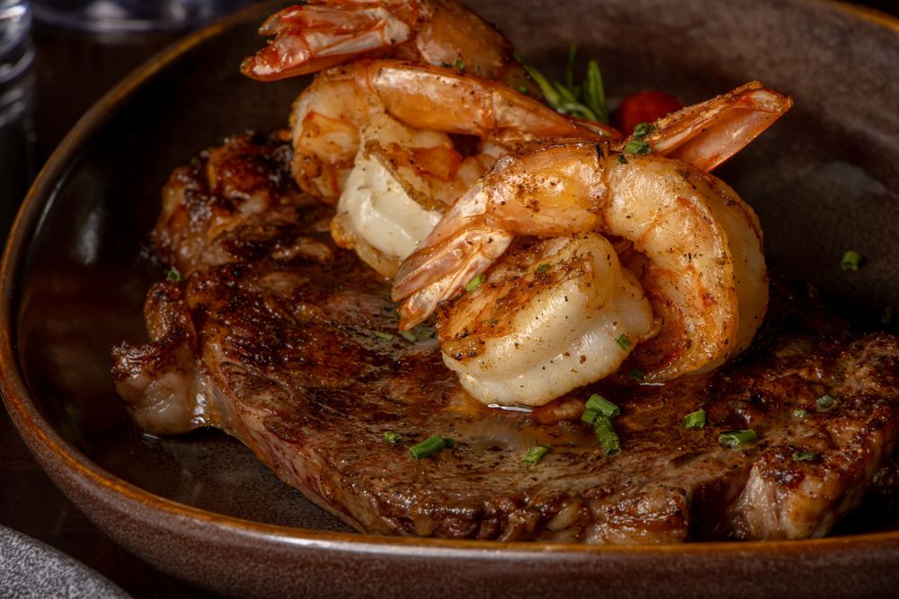 Surf and turf dish featuring grilled steak and shrimp on a dark plate. By NJ Photographer Andrew Fein