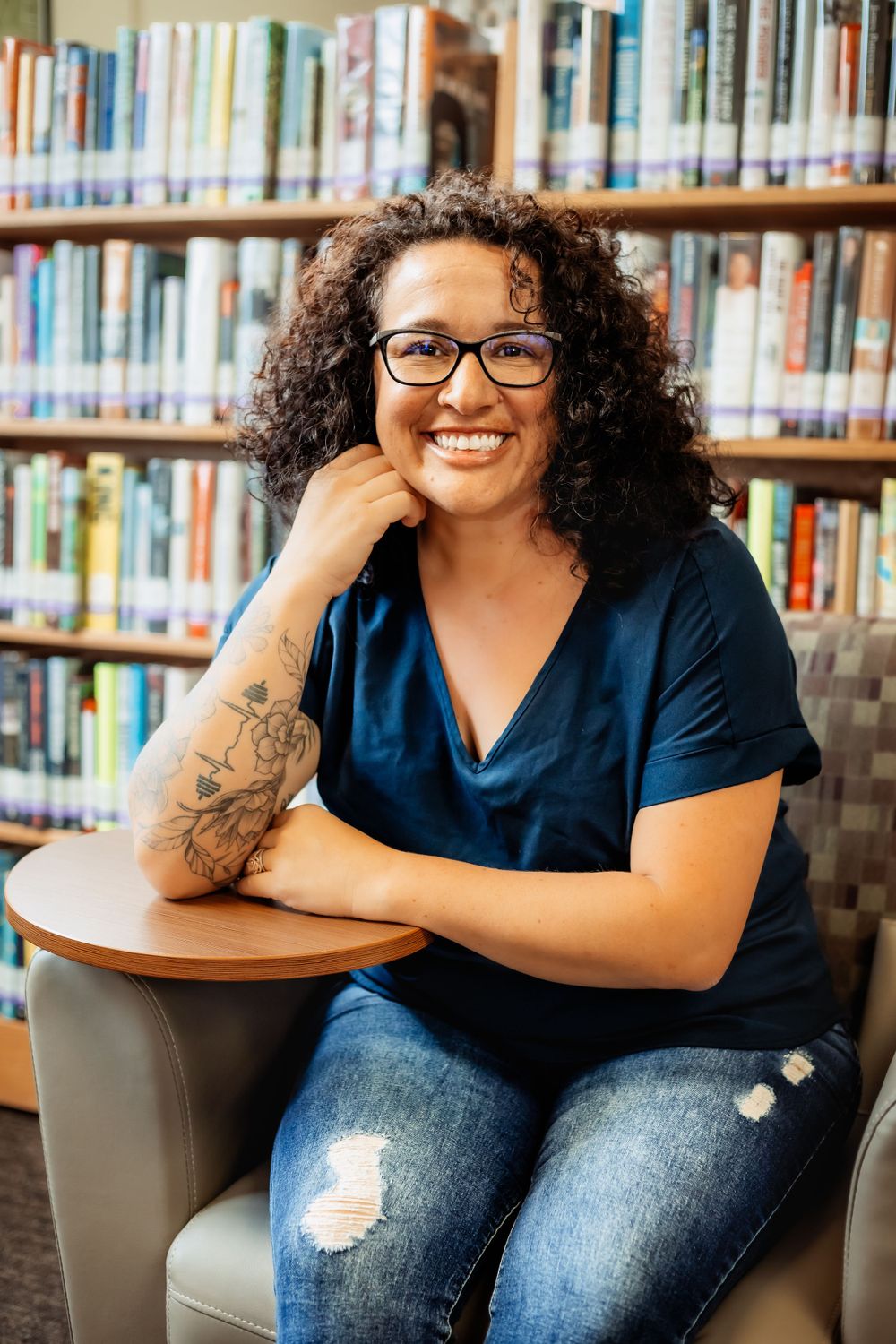 Person sitting in library with bookshelf background showing warm genuine smile.