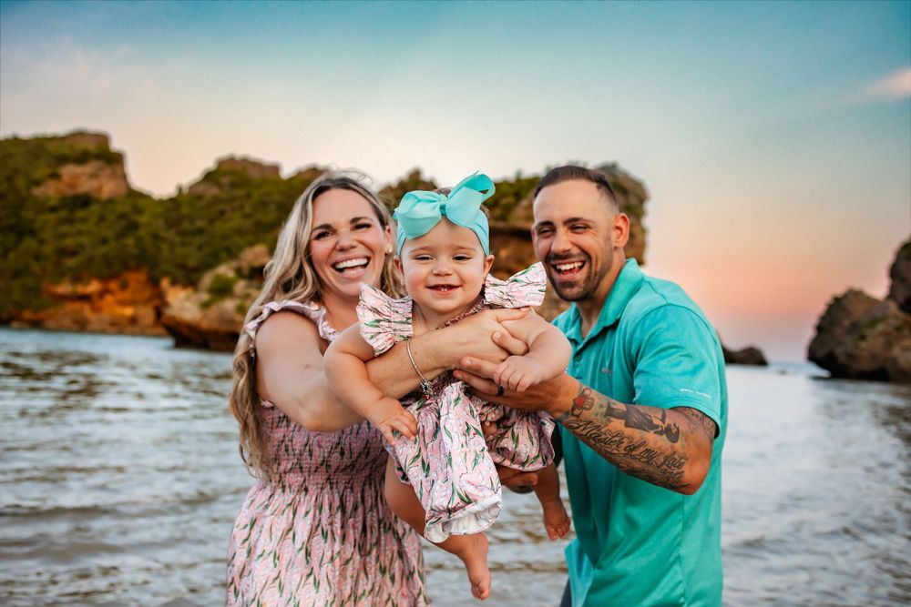 Happy family laughing together on beach at sunset with coastal rocks in background.