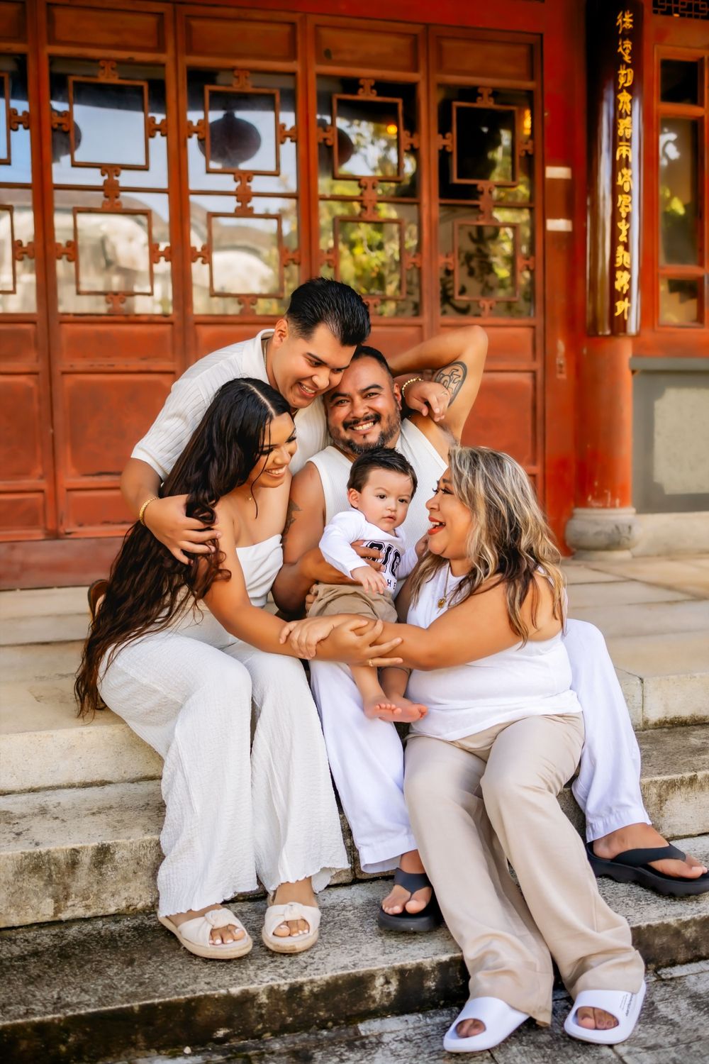 Family dressed in white sitting together on steps of traditional Chinese building.