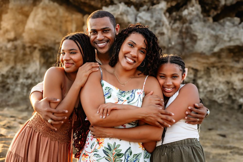 A joyful group embrace on a beach with rocky cliffs in the background.