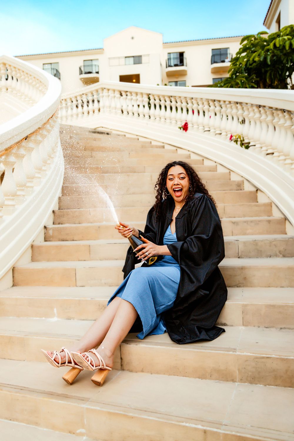 Graduate celebrating on grand white stone stairs outdoors while wearing traditional graduation attire.