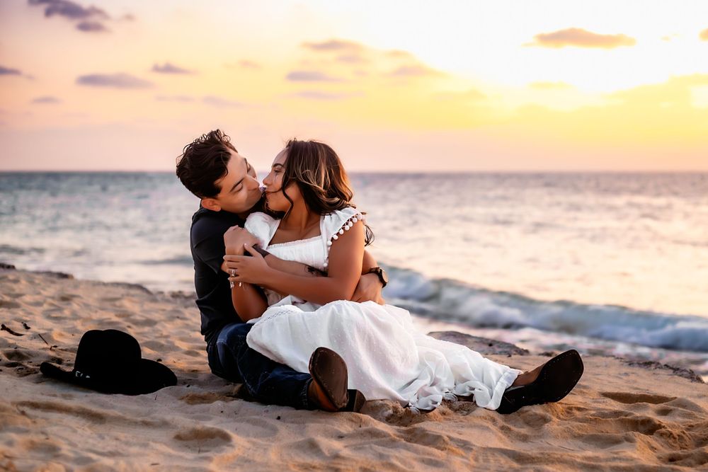 A romantic sunset beach scene with a couple embracing on the sand as waves roll in along the shoreline.