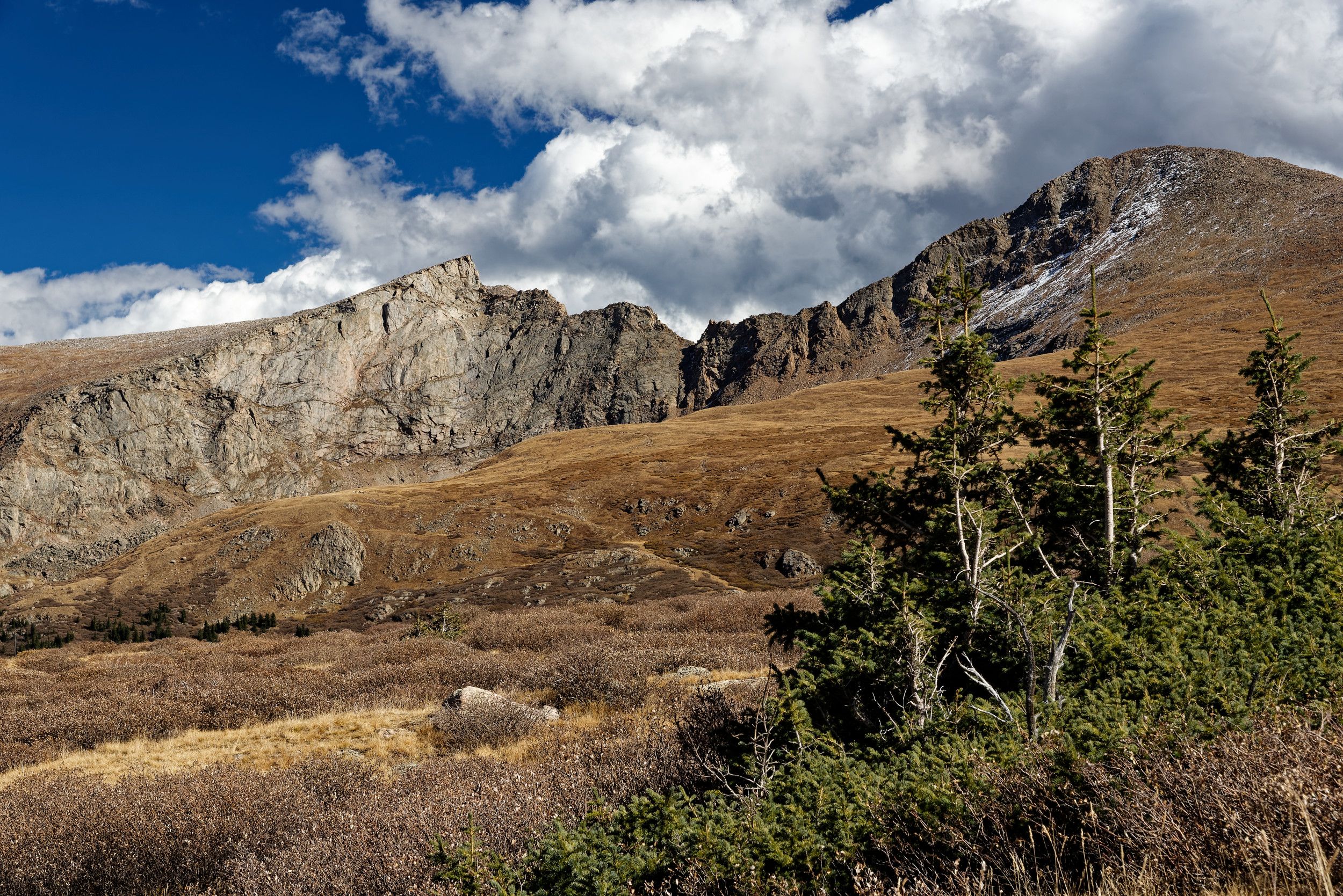 Scenic mountain landscape with rugged peaks and rocky cliffs under dramatic cloudy skies.