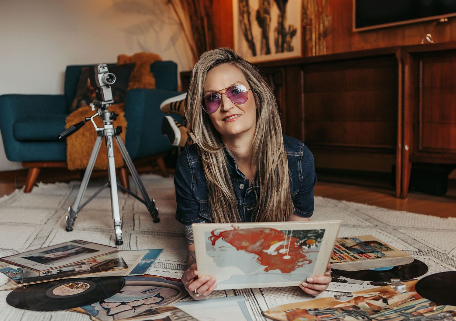 Photographer reviewing printed photos while sitting on floor with camera equipment.