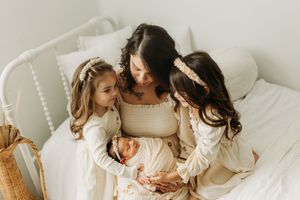 Family sharing tender moments together while relaxing on white bedding in natural light.
