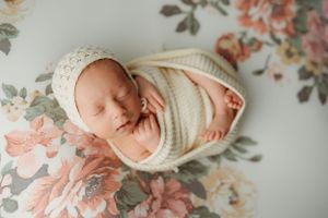 Newborn photography setup with floral backdrop and cream-colored wrapping.