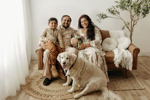 Family of three with golden retriever dog posing on brown leather sofa in bright minimalist living room.
