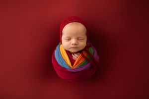 Professional newborn photography setup with deep red background and soft lighting.