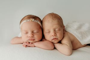 Artistic newborn portrait showing sleeping twins under soft white blanket.