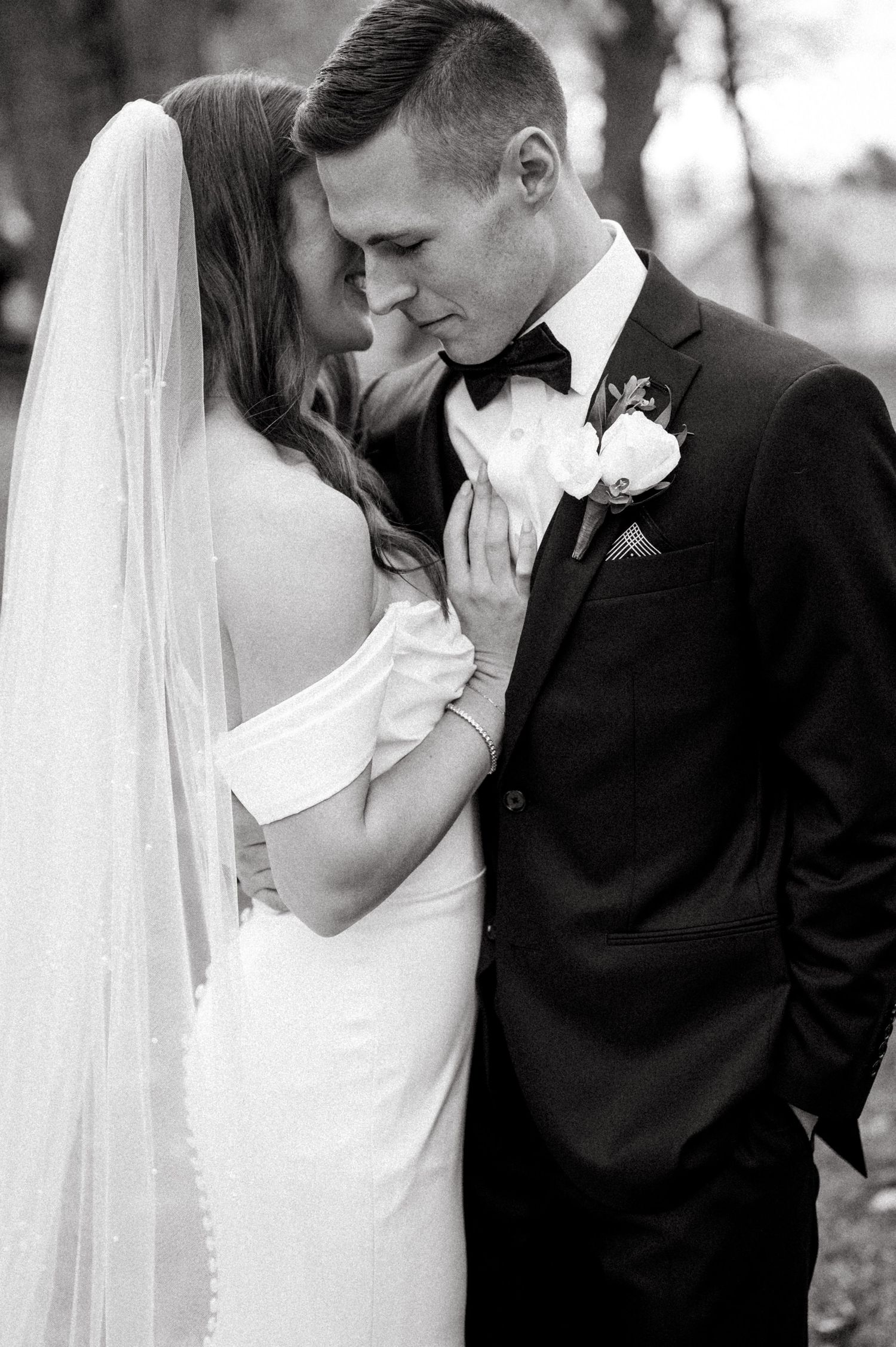 Intimate black and white wedding photo of a couple sharing a tender moment in their formal attire.