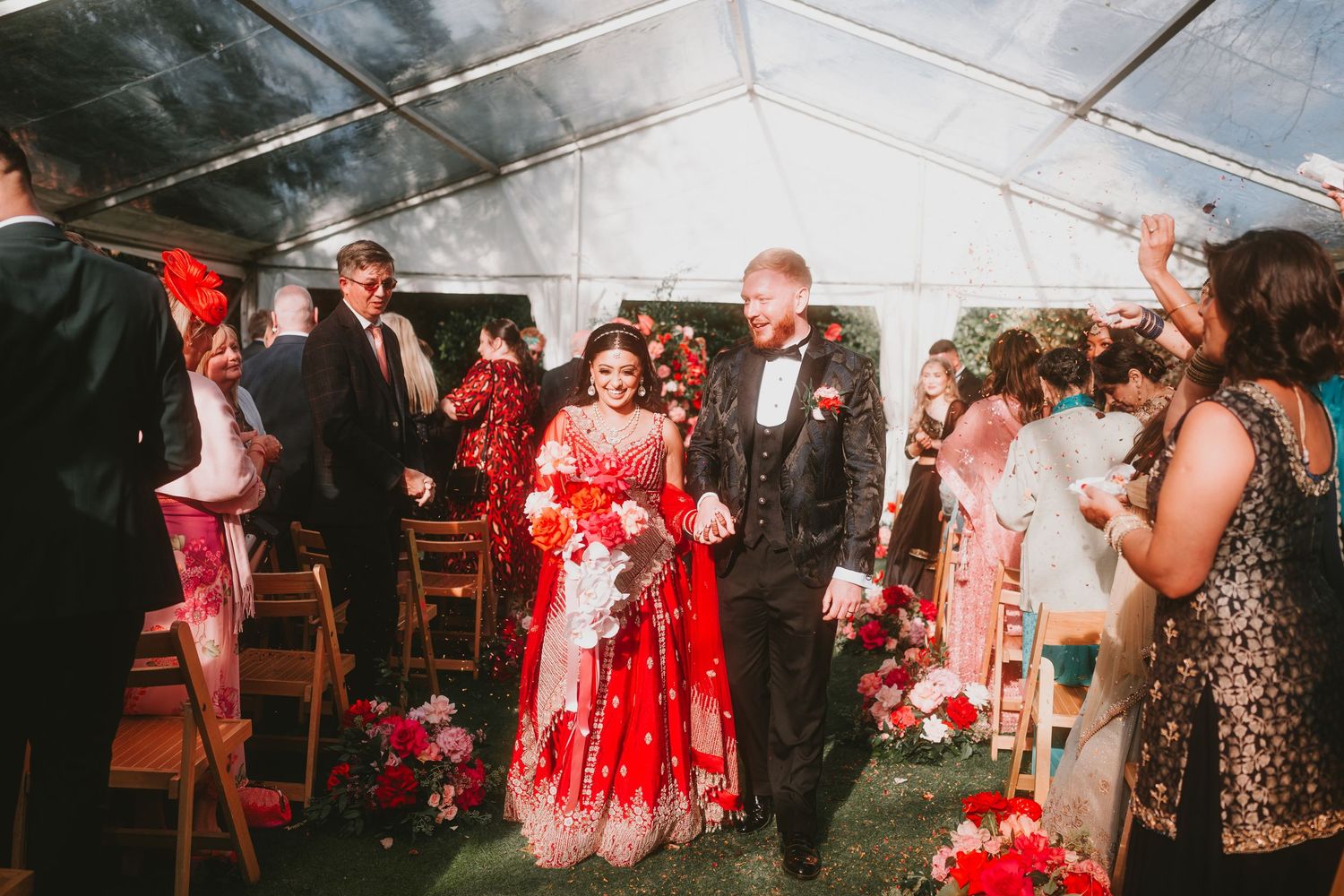 Wedding guests celebrating in a tent with red floral decorations and formal attire.