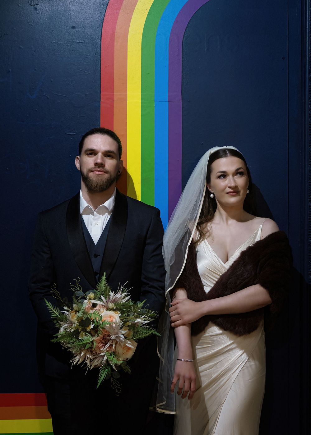 A series of wedding portraits against a dark wall with rainbow stripe backdrop featuring a bouquet of flowers.