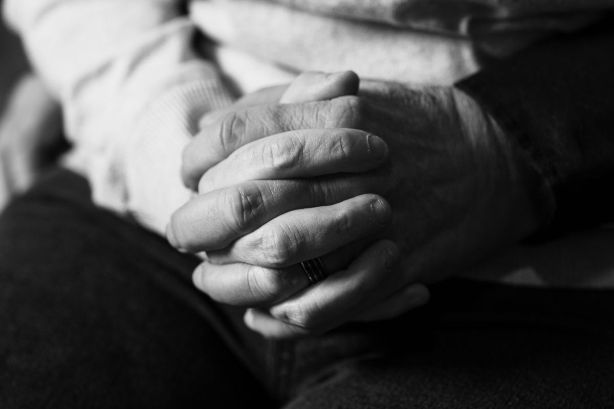 Black and white close-up photo of clasped hands resting on fabric.