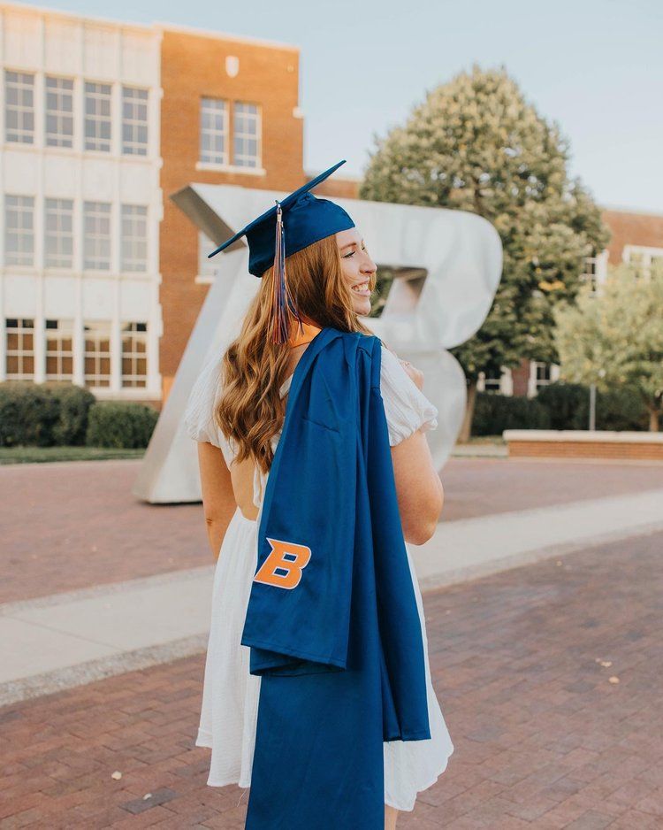 Graduate wearing blue cap and gown stands in front of large number sculpture on university campus during commencement.