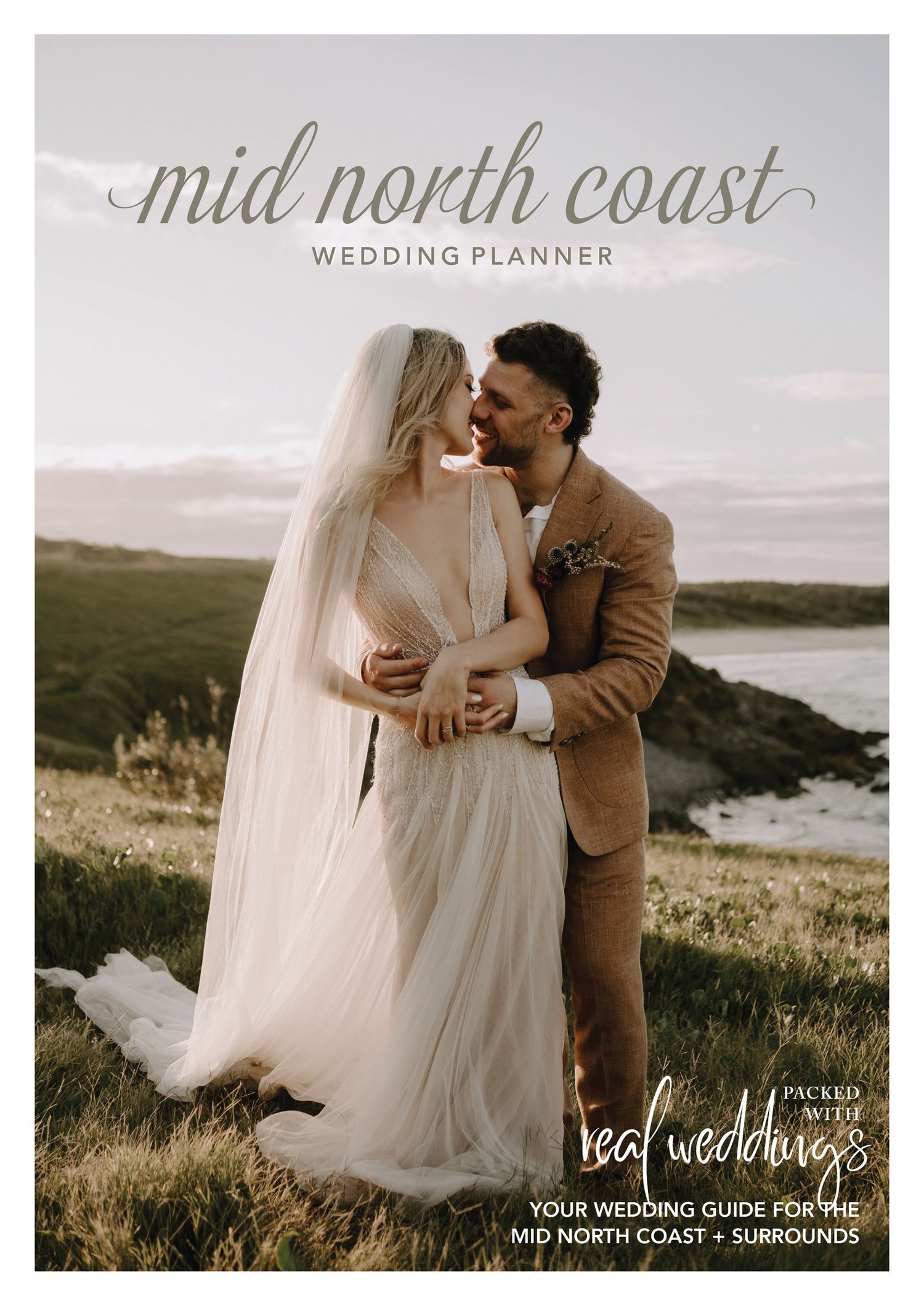 Romantic coastal wedding photoshoot at sunset with flowing white dress and brown suit against dramatic cliffside backdrop.