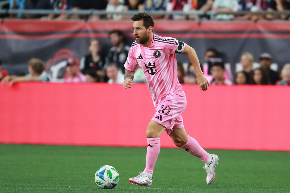 Soccer players in pink jerseys compete for possession during an intense match on a grass field.