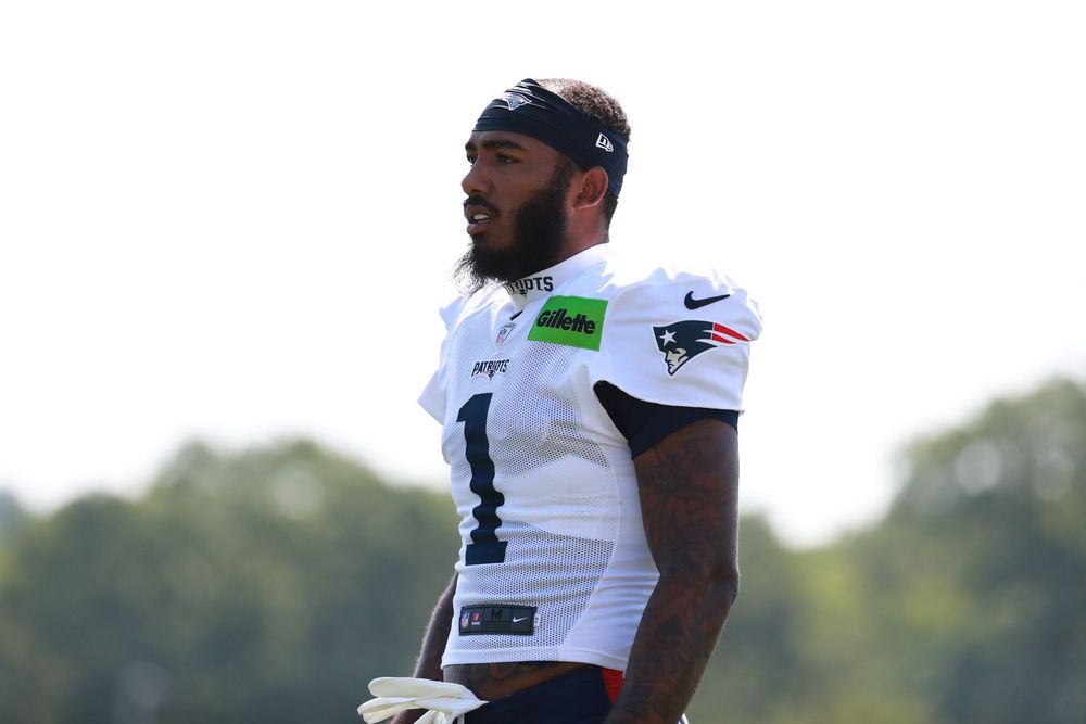 Football players in practice gear stand on the sidelines during training camp.
