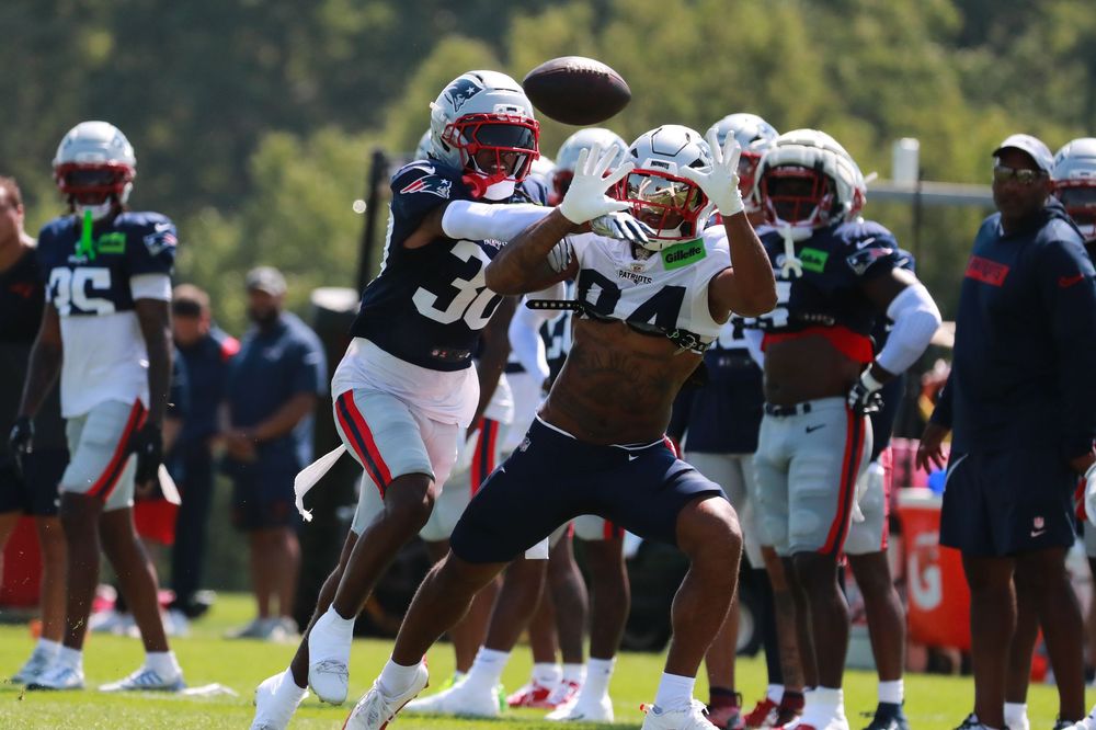 Football players line up in practice formation on a sunny training field.