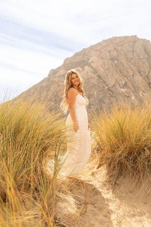 Woman in white dress poses in front of dramatic mountain landscape with golden beach grass.