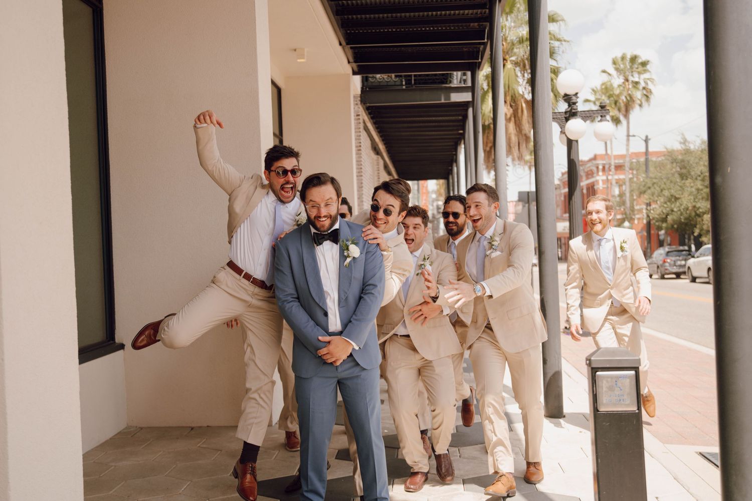 A group of people in light colored clothing running and laughing together in a covered walkway.