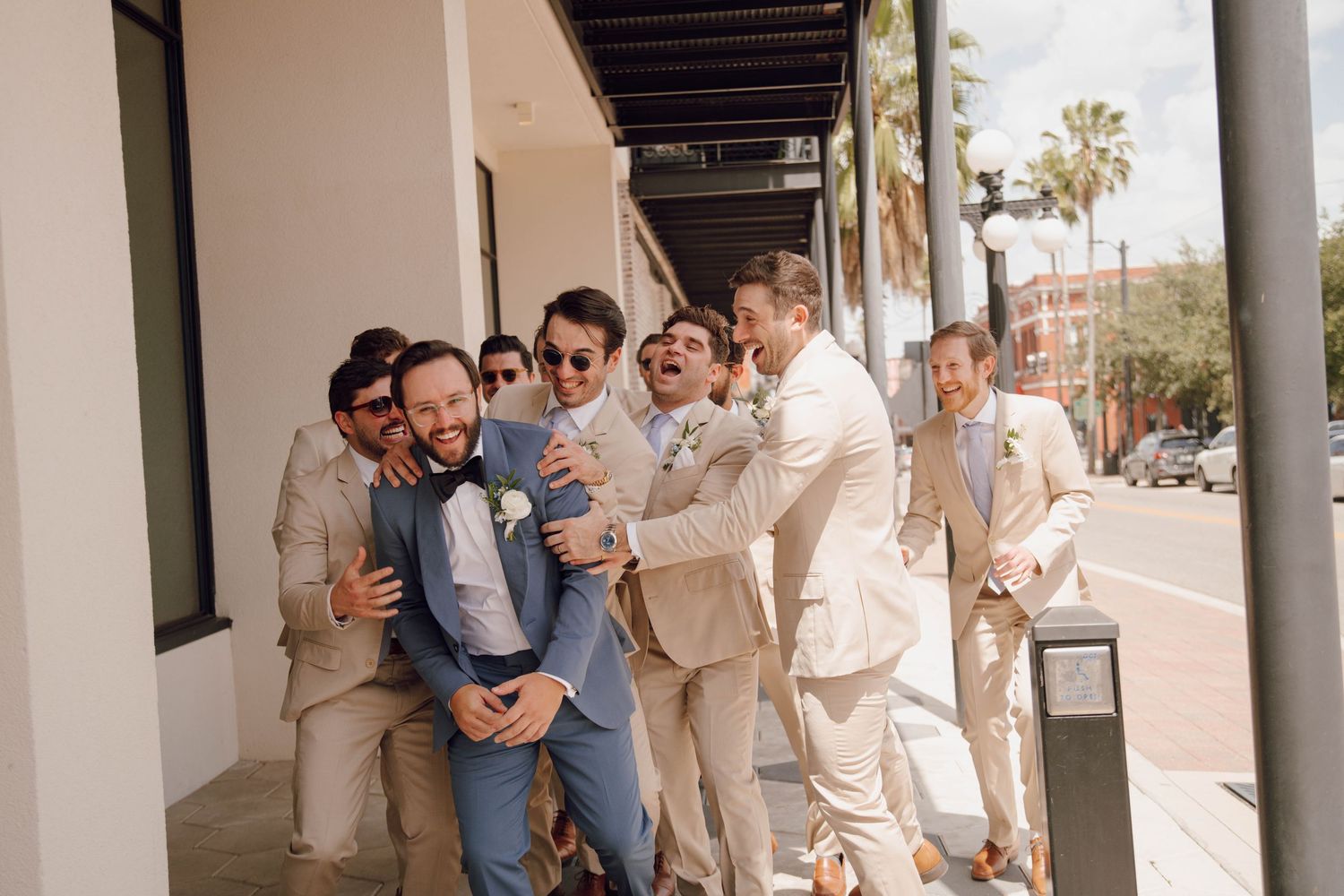 Wedding party in cream colored attire poses together under a covered outdoor walkway.