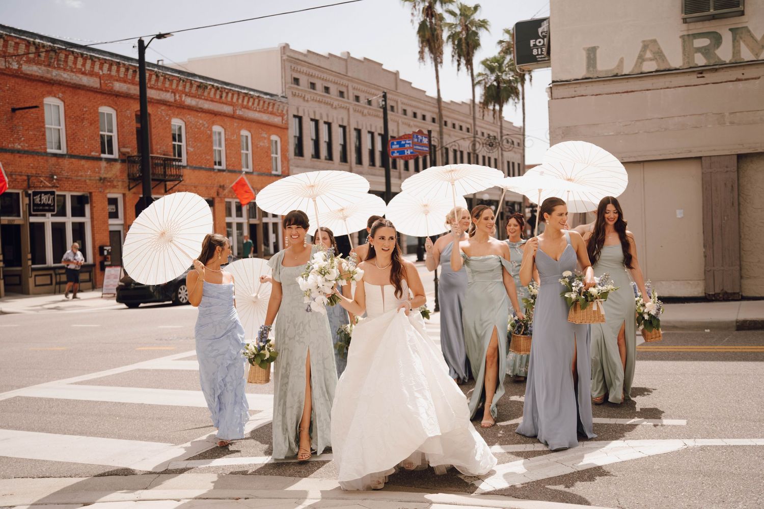 A panoramic collage of a wedding party walking down a brick-lined street with parasols and formal attire.