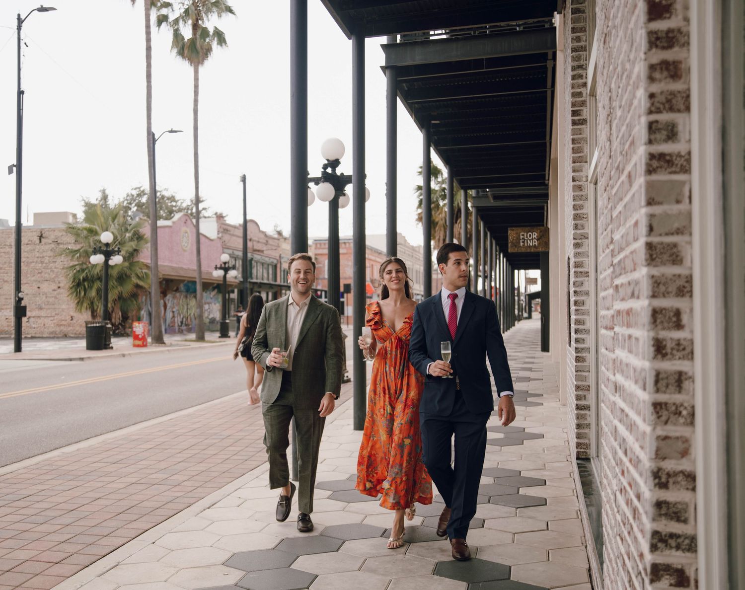 Wedding party walks along a covered brick walkway with arched columns.