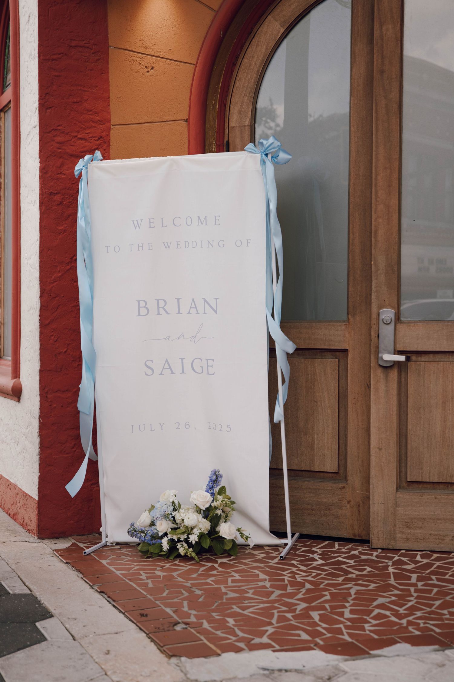 Welcome sign with floral decorations displayed outside a brick building entrance.