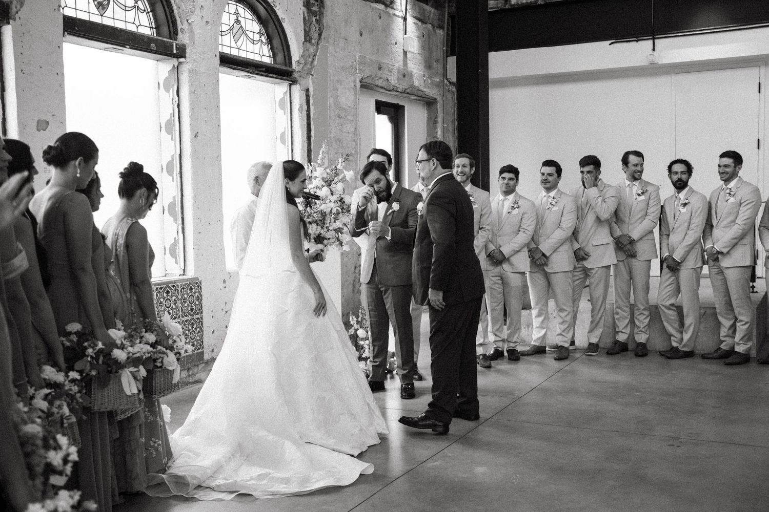 Black and white photo of a wedding ceremony in a rustic indoor venue with exposed brick walls.