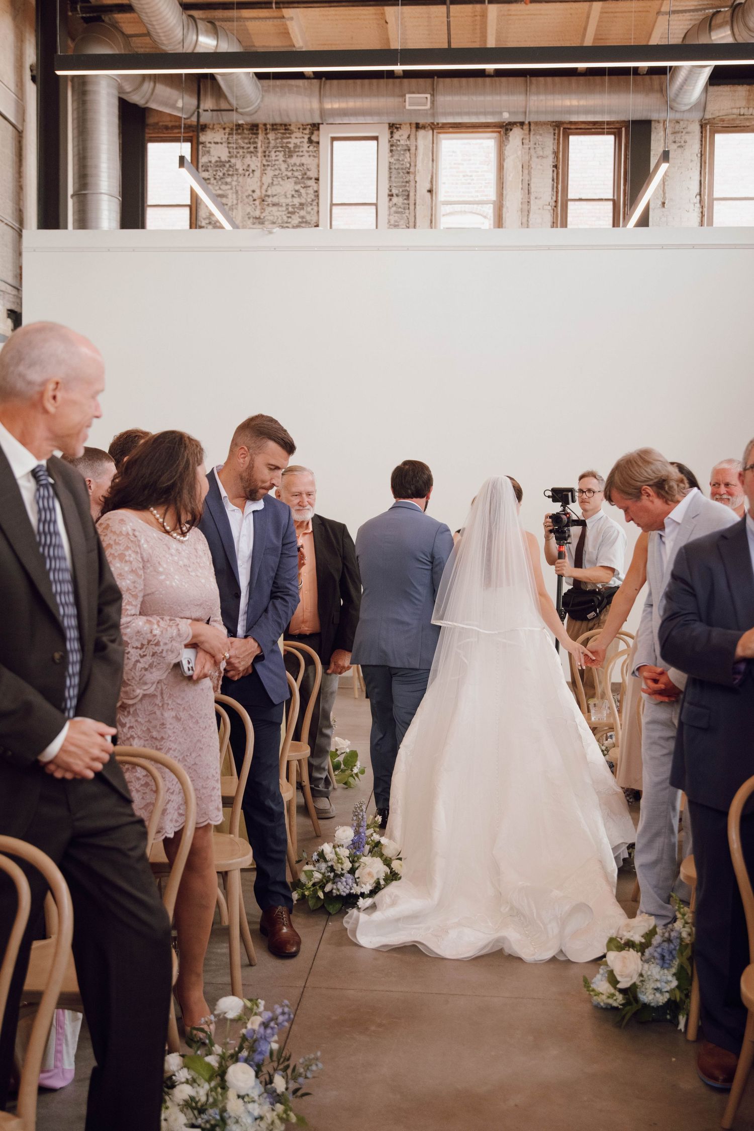 Wedding reception in a rustic venue with guests mingling around floral arrangements.