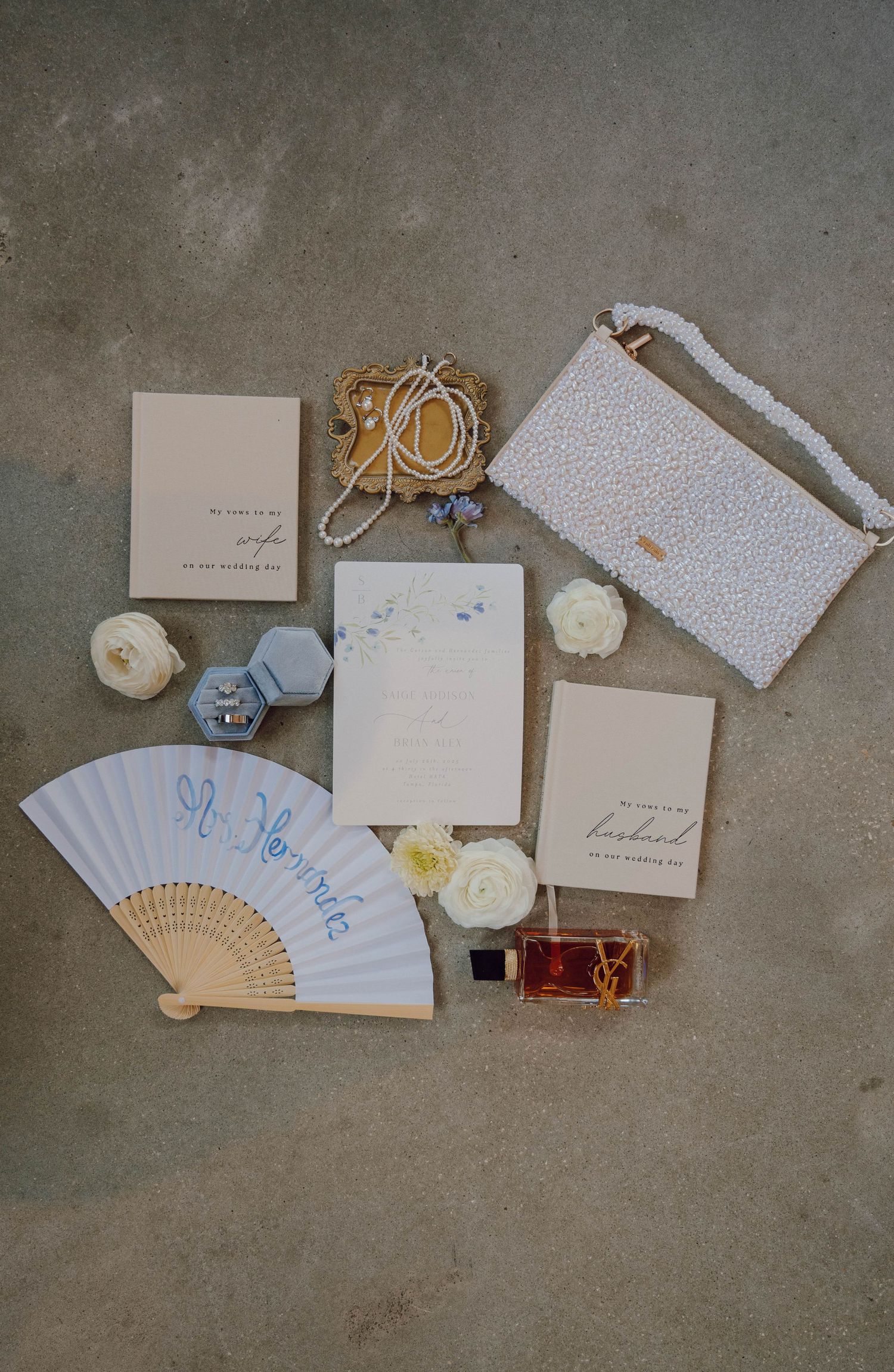 Wedding stationery collection with delicate paper fans, floral accents, and elegant invitations arranged on a concrete surface.