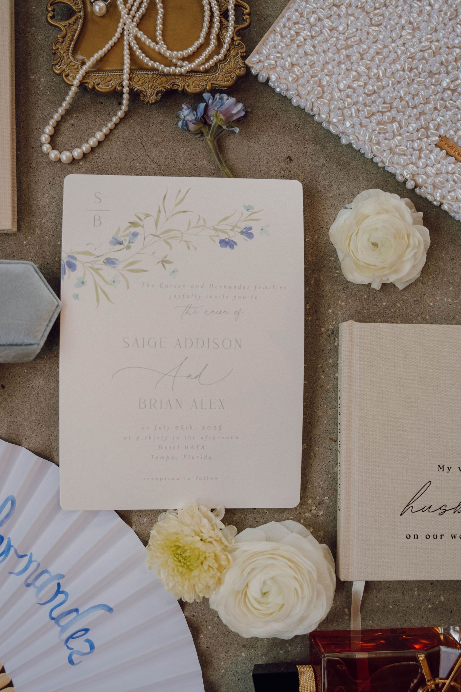Wedding invitation cards and white roses arranged on a gray surface with delicate calligraphy details.