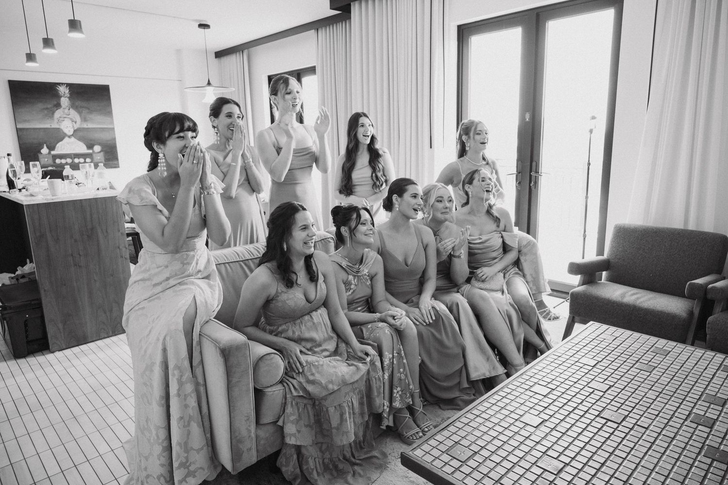 A group in matching gray dresses sits together watching something off camera with excited expressions.