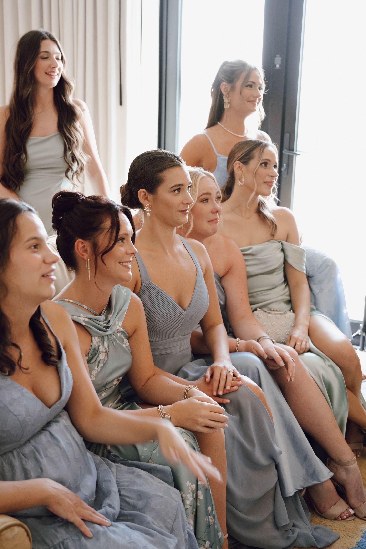 A group of bridesmaids in matching gray dresses sit together and laugh during a wedding celebration.