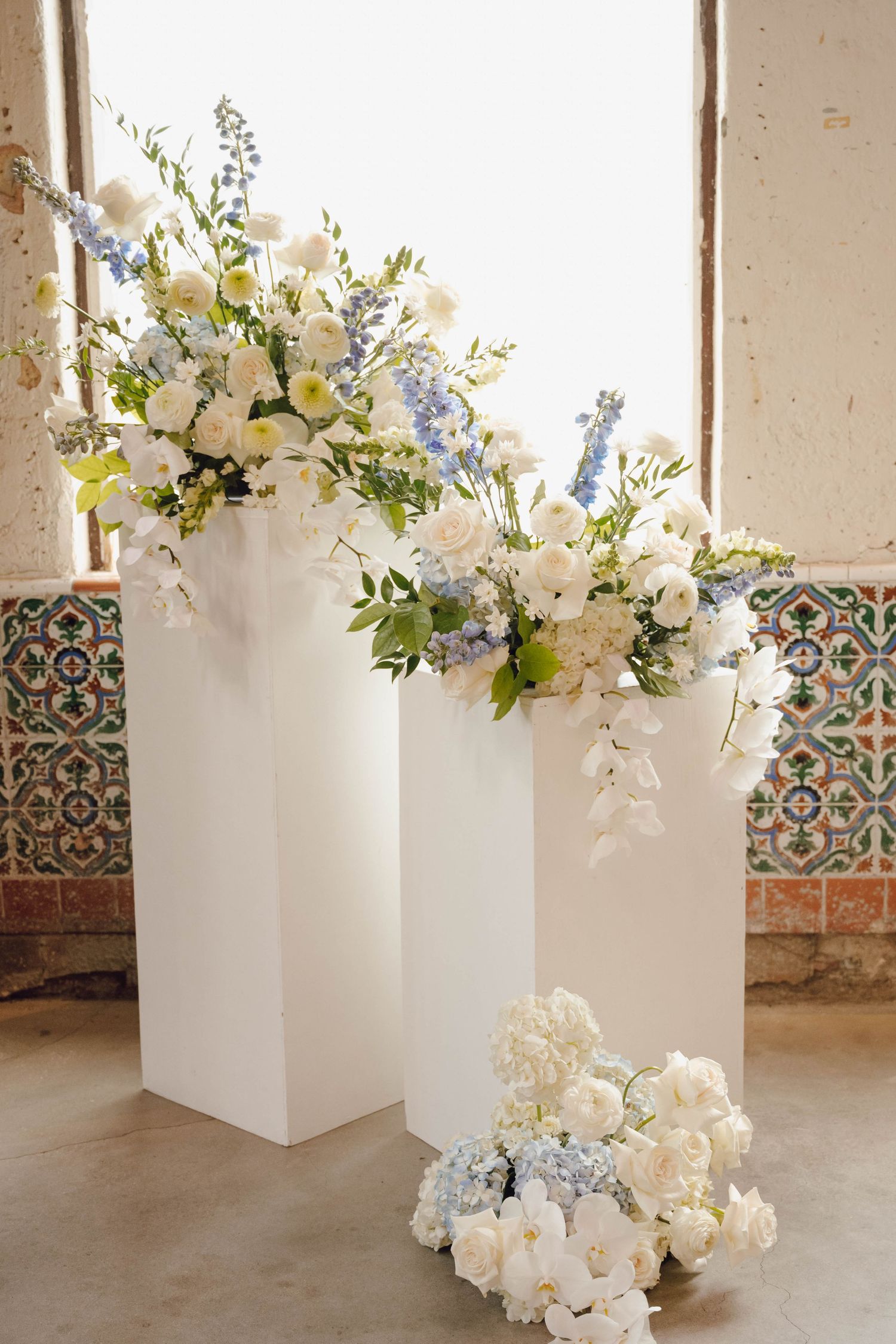 White floral arrangements in modern cube vases create an elegant display against a neutral backdrop with decorative tiles.