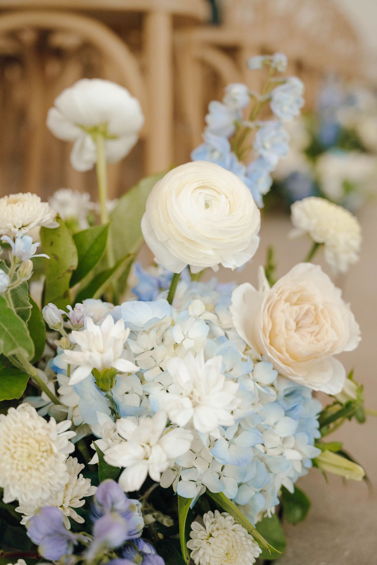 Elegant white and pale blue floral centerpiece featuring hydrangeas, ranunculus, and roses in a romantic garden style.