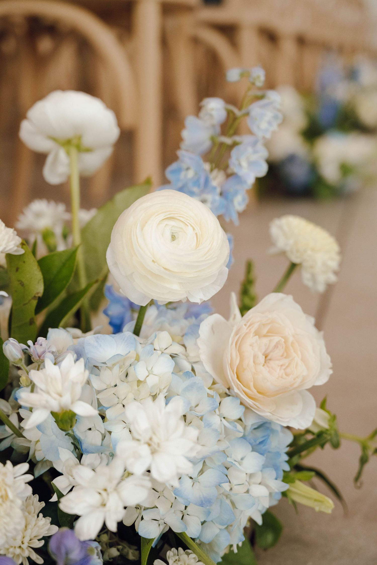 Elegant floral arrangement featuring white ranunculus, pale blue hydrangeas, and delicate blooms in a soft pastel palette.