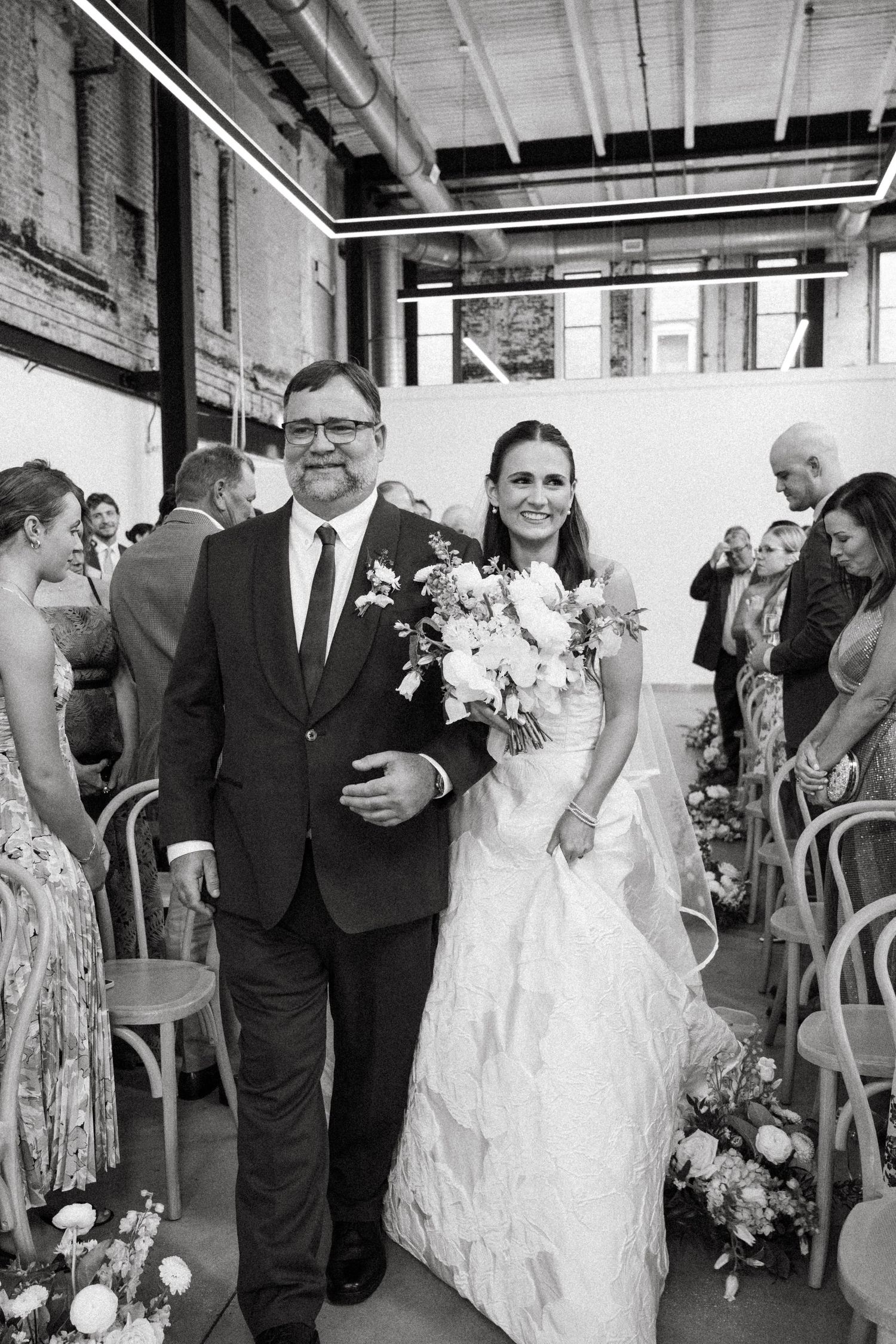 Wedding processional in an industrial-style venue with exposed beams and brick walls.