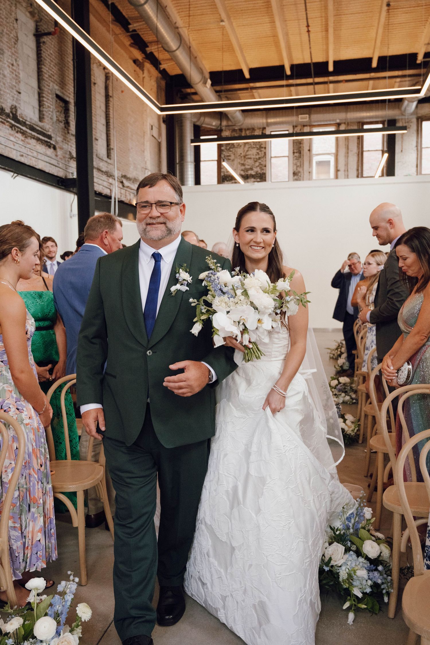 Wedding ceremony procession in a modern industrial venue with wooden ceiling beams.