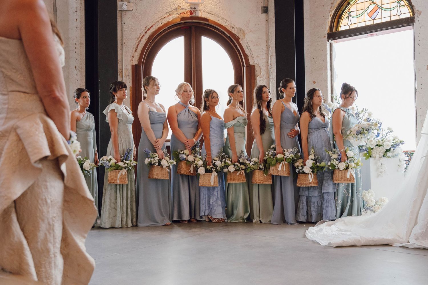 Wedding party members in gray and white attire posed in front of arched windows.