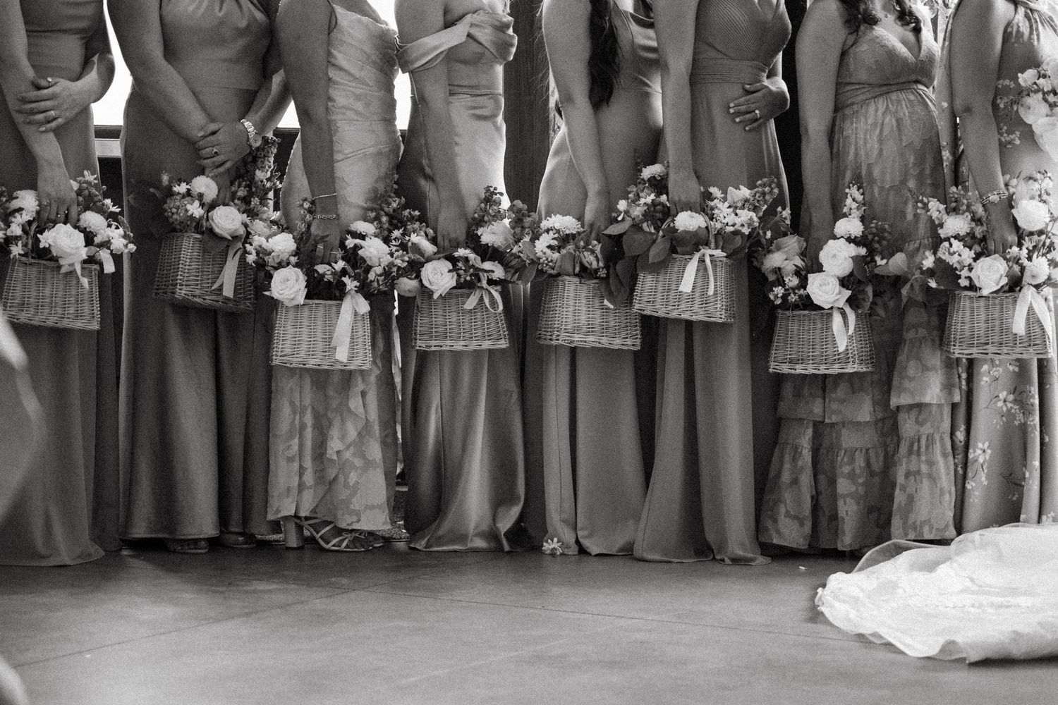 Wedding party members lined up in gray dresses and tan suits in front of a brick wall.
