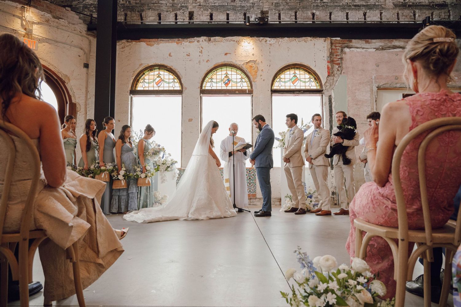 Wedding ceremony setup in an industrial brick venue with arched windows and natural light.