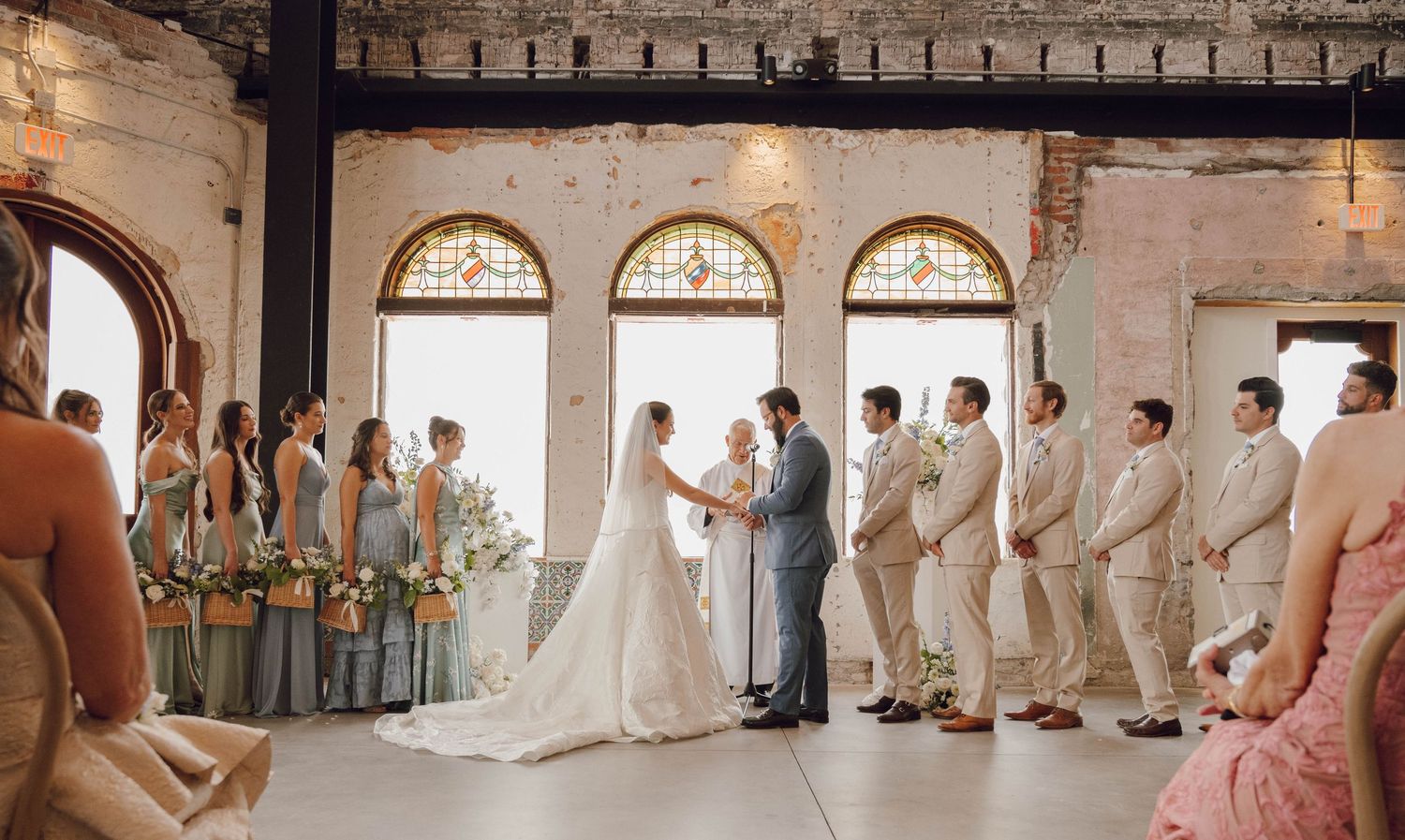 Panoramic view of wedding ceremony in rustic brick venue with guests and wedding party lined up.