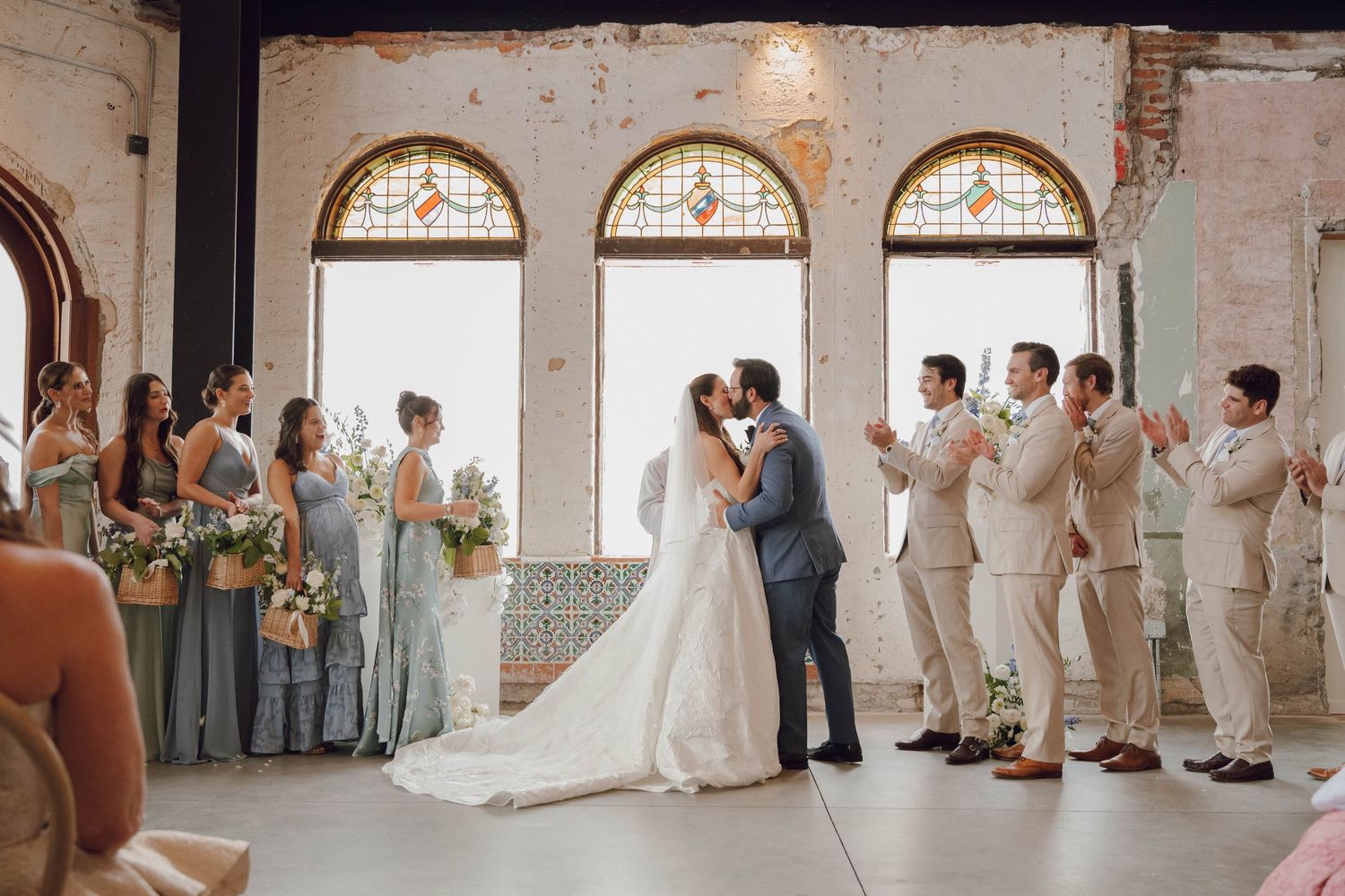 Wedding party poses in front of exposed brick walls and arched windows.