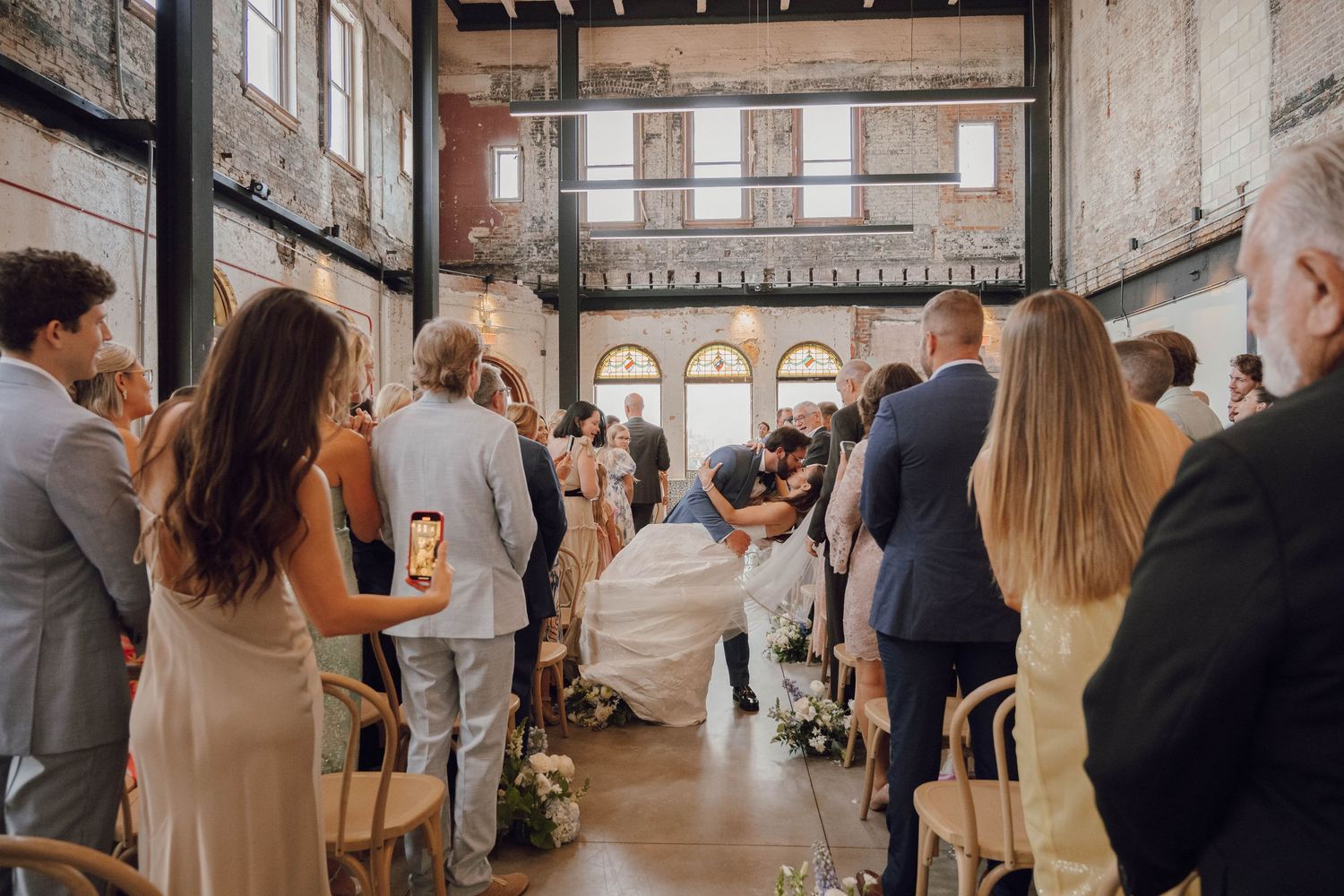 Wedding guests gathered in a historic brick venue with high ceilings and natural lighting.