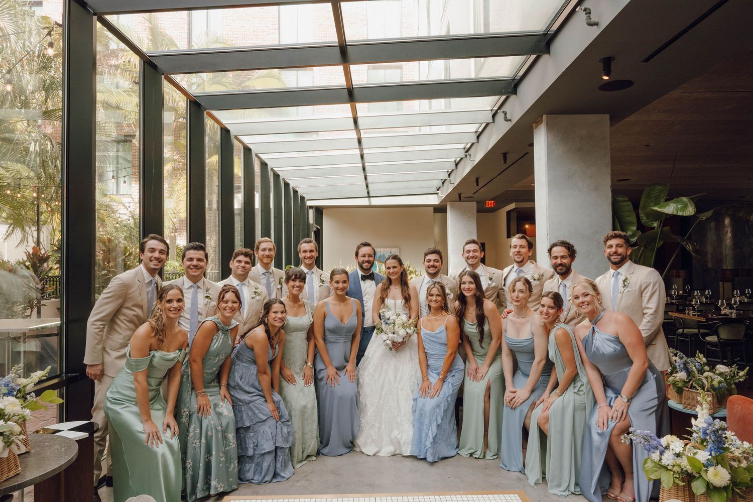 Wedding party in light blue bridesmaid dresses poses together in an elegant indoor venue.