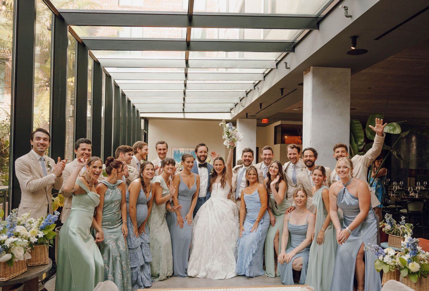 Wedding party in light blue bridesmaid dresses poses together in an elegant covered outdoor corridor.